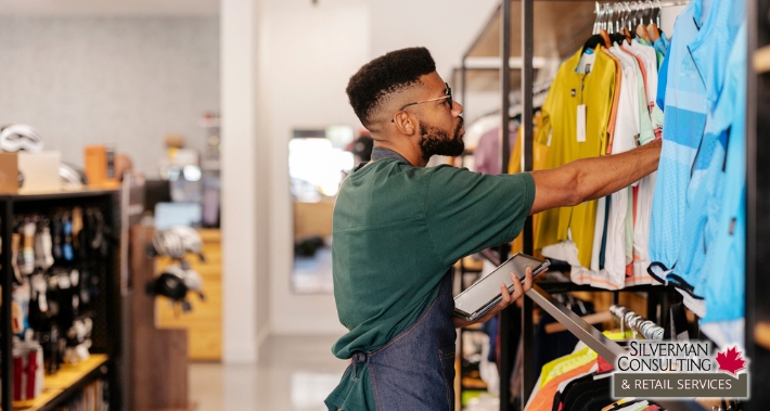 Retail store employee using a tablet while checking and organizing clothing inventory on display racks. | Silverman Consulting & Retail Services | Retail Sales Consultants Going Out Of Business Sale Retirement Sale Store Moving Store Closing Sale Consultants